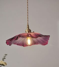 a light that is hanging from a ceiling with flowers in the vases behind it