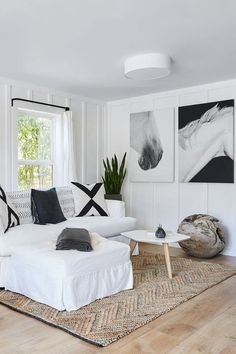 a living room filled with white furniture and paintings on the wall above it's windows