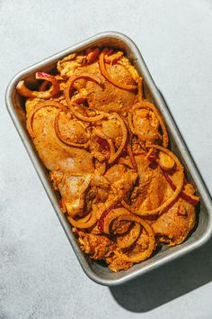 a casserole dish with meat and onions in it on a white table top