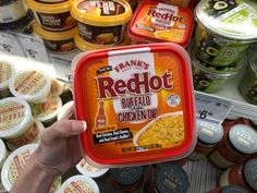 a person holding up a container of red hot buffalo chicken soup in front of other food items