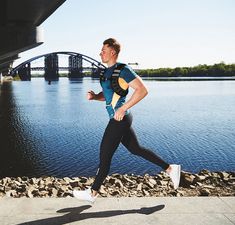 a man is running by the water with a bridge in the background