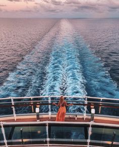 a woman standing on the back of a boat looking out at the ocean in the distance