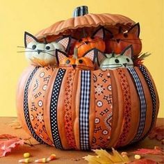 two cats sitting in a pumpkin shaped basket on top of a wooden table with autumn leaves