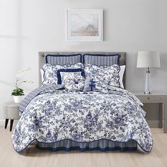 a bed with blue and white comforters in a room next to a lamp on a table