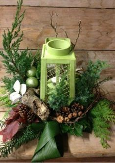 a green lantern surrounded by greenery, pine cones and other holiday decorations on a wooden table