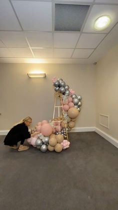 a woman standing next to a ladder with balloons on it in an empty room filled with people