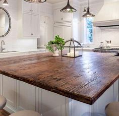 a large wooden counter top in a kitchen next to stools and an island with lights