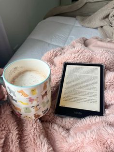 a person is holding a book and a cup of coffee on a bed with a pink blanket