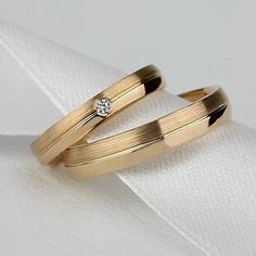 two gold wedding bands with a diamond in the middle on top of a white cloth