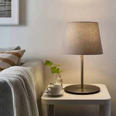 a small table with a lamp on it and a coffee cup next to it in front of a couch