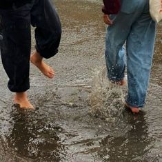 two people are walking in the water with their shoes on and one person is holding an umbrella