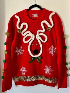 a red sweater with white snowflakes and a reindeer face on it, hanging from a door