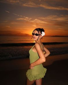 a woman standing on top of a beach next to the ocean at sun set with her hair in a bun