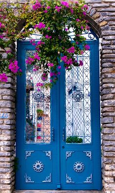 a blue door with pink flowers hanging over it's glass doors and brick wall