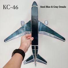 a hand is holding up a metal model of a blue and grey jet plane with its wings spread out