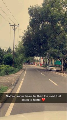 an image of a road with trees and cars on both sides, in the distance is a sign that says nothing more beautiful than the road that leads to home