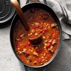 a pot filled with meat and bean stew on top of a table next to a wooden spoon