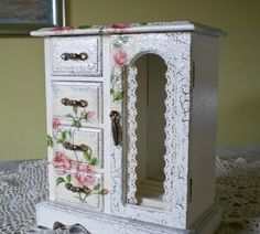 an ornate white cabinet with flowers painted on the doors and drawers is sitting on a lace doily tablecloth