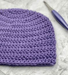 a crocheted purple hat sits next to a pair of scissors