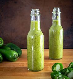 two bottles filled with green sauce next to peppers