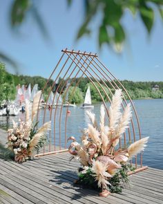 there are two vases with flowers and plants on the wooden dock by the water