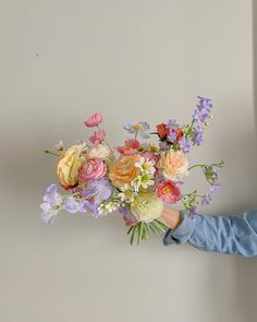 a person holding a bouquet of flowers in their hand and looking at the wall behind them