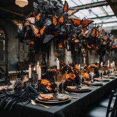 a dining table set with black and gold plates, napkins, candles and butterfly centerpieces