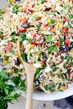 a white bowl filled with rice salad and wooden spoons next to parsley on the side