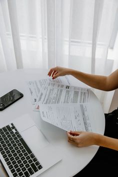 a woman is sitting at a table with papers in front of her and a laptop