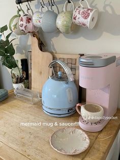 there is a tea kettle and cups on the counter next to a cup holder with mugs hanging from it