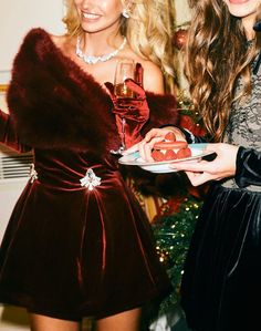 two beautiful women standing next to each other in front of a christmas tree holding wine glasses