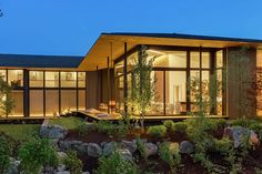 a modern house is lit up at night with lights on the windows and landscaping around it