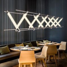 a restaurant with wooden tables and chairs in front of a black wall that has lights hanging from the ceiling