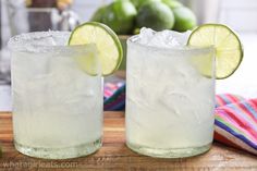 two glasses filled with ice and limes sitting on a table next to each other