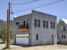 a two story house sitting on top of a dirt lot next to a mountain range