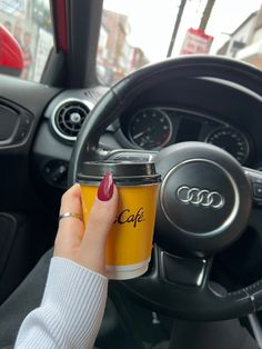 a woman is holding a coffee cup in her car