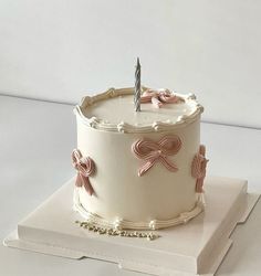 a white cake with pink bows and a single candle sitting on top of a book