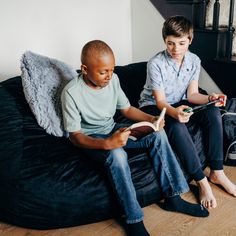 two young boys sitting on a black couch reading books while one boy looks at the camera