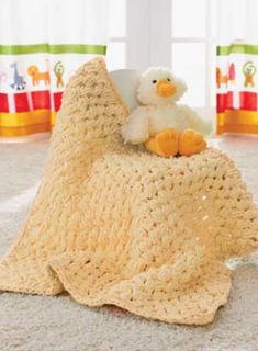 a crocheted blanket on the floor with a stuffed duck sitting on top of it