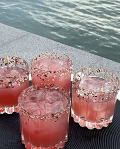 three glasses filled with pink liquid sitting on top of a black tray next to water