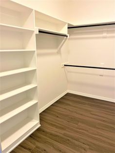 an empty closet with white shelves and wood flooring