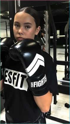 a woman wearing black boxing gloves in a gym with her hand on the punching mitt