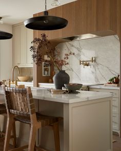 a kitchen with marble counter tops and wooden chairs in front of an island that has a vase on it