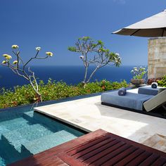 an outdoor pool with lounge chairs and umbrellas next to the ocean on a sunny day