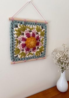 a crocheted flower is hanging on the wall next to a vase with flowers