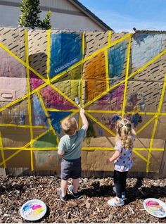 two young children are painting on a wall with yellow tape and paper plates in front of them