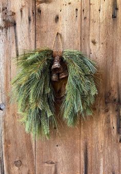 a pine cone wreath hanging on the side of a wooden door with an old fashioned bell