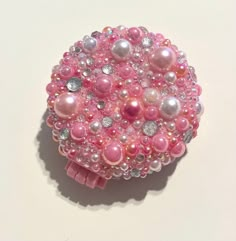 a pink and white brooch with pearls on it's side, sitting on a table