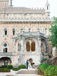 a bride and groom are standing in front of an old building with stone steps leading up to it