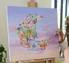 a woman is painting on an easel with butterflies in the sky and clouds behind her